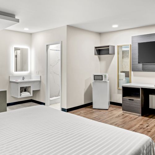 The image shows a hotel room with a bed, TV, small fridge, sink, desk, and a red jacuzzi tub. The decor is modern and minimalistic.