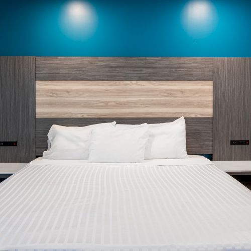 A neatly made bed with white pillows and linens, surrounded by a modern gray and blue-themed headboard and room decor.