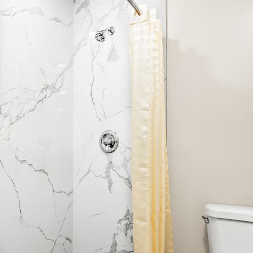 Bathroom with marble walls, shower curtain, shower head, and white toilet. Clean and simple design.