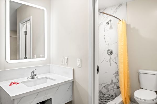 A modern bathroom features a marble sink, illuminated mirror, yellow shower curtain, and toilet within a clean, minimal design.