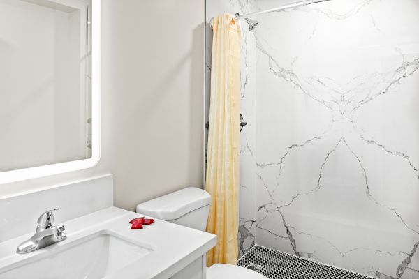 A modern bathroom features a white sink, toilet, marble shower with a yellow curtain, and circular floor tiles.