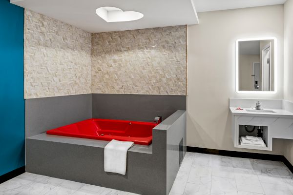 A room with a large red bathtub, tiled walls, a towel, and a modern sink with a mirror.