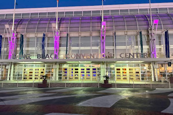 The image shows the exterior of the Long Beach Convention Center, with purple lighting illuminating the front entrance.