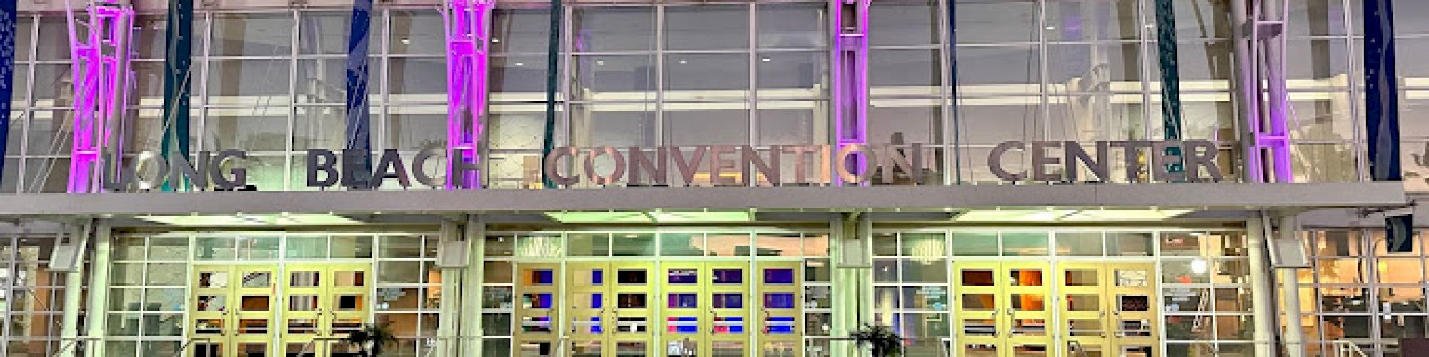 The image shows the Long Beach Convention Center entrance, with glass windows and purple lights illuminating the facade.