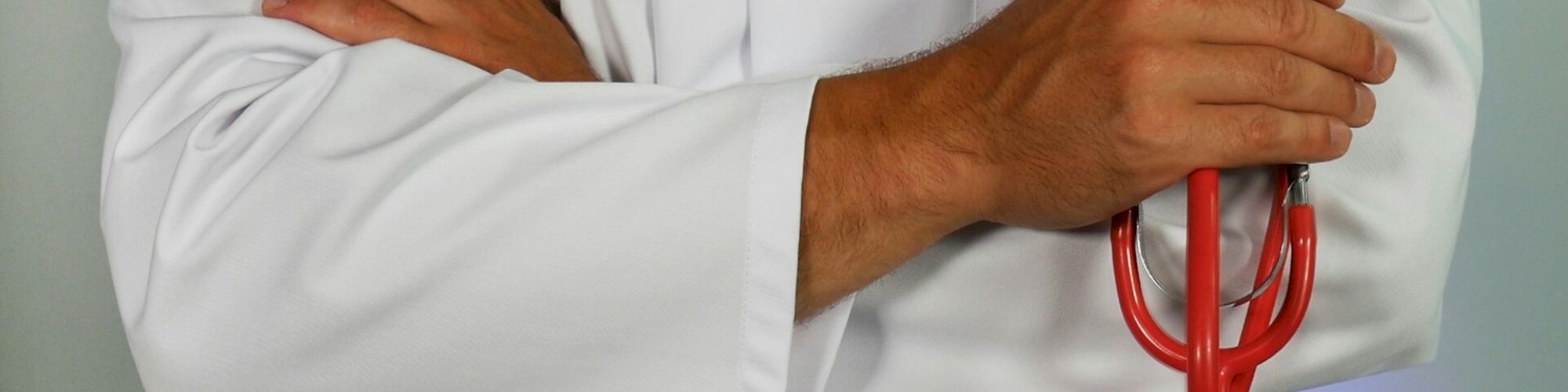 A person in a white coat holding a red stethoscope, arms crossed.