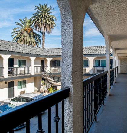 The image shows a motel with parked cars, palm trees, exterior corridors, and a railing with columns.